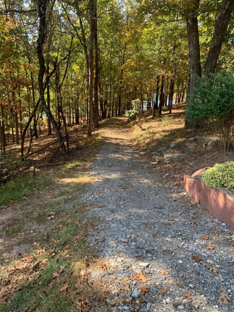 Gravel driveway sloping downhill through autumn trees toward the lake