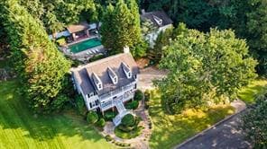 Aerial view of a white two-story home with a backyard pool surrounded by trees