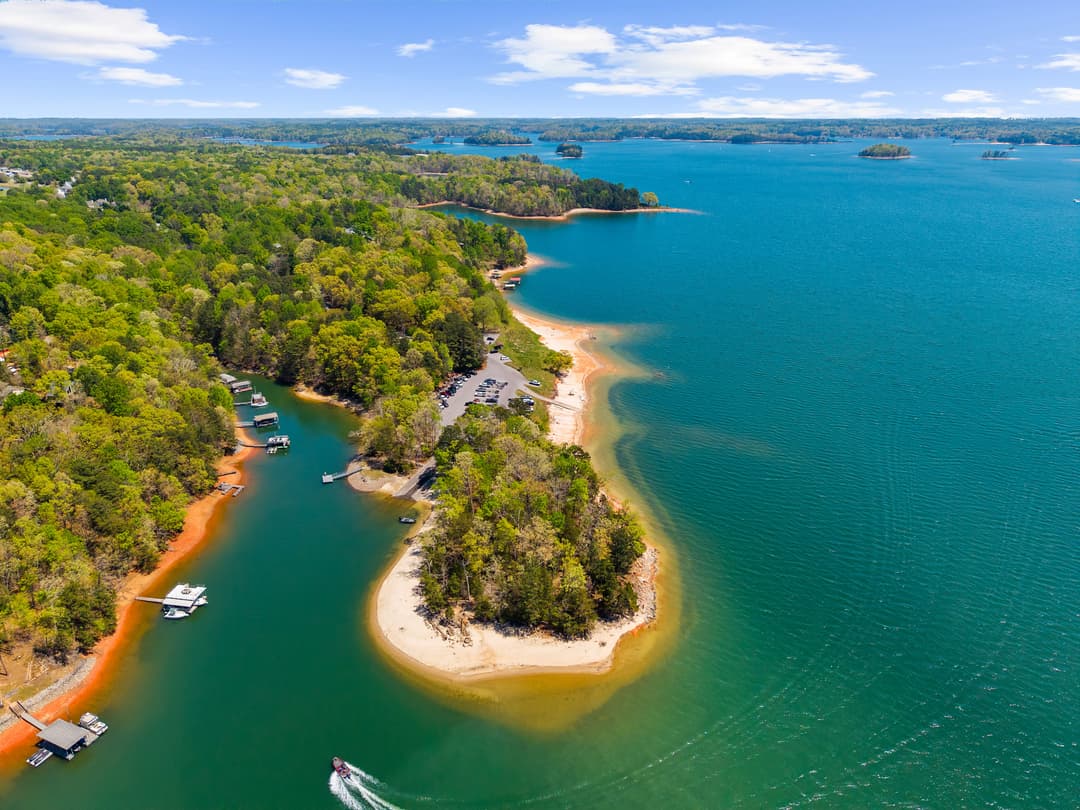 Aerial view showing the home, lakeshore, and surrounding wooded privacy